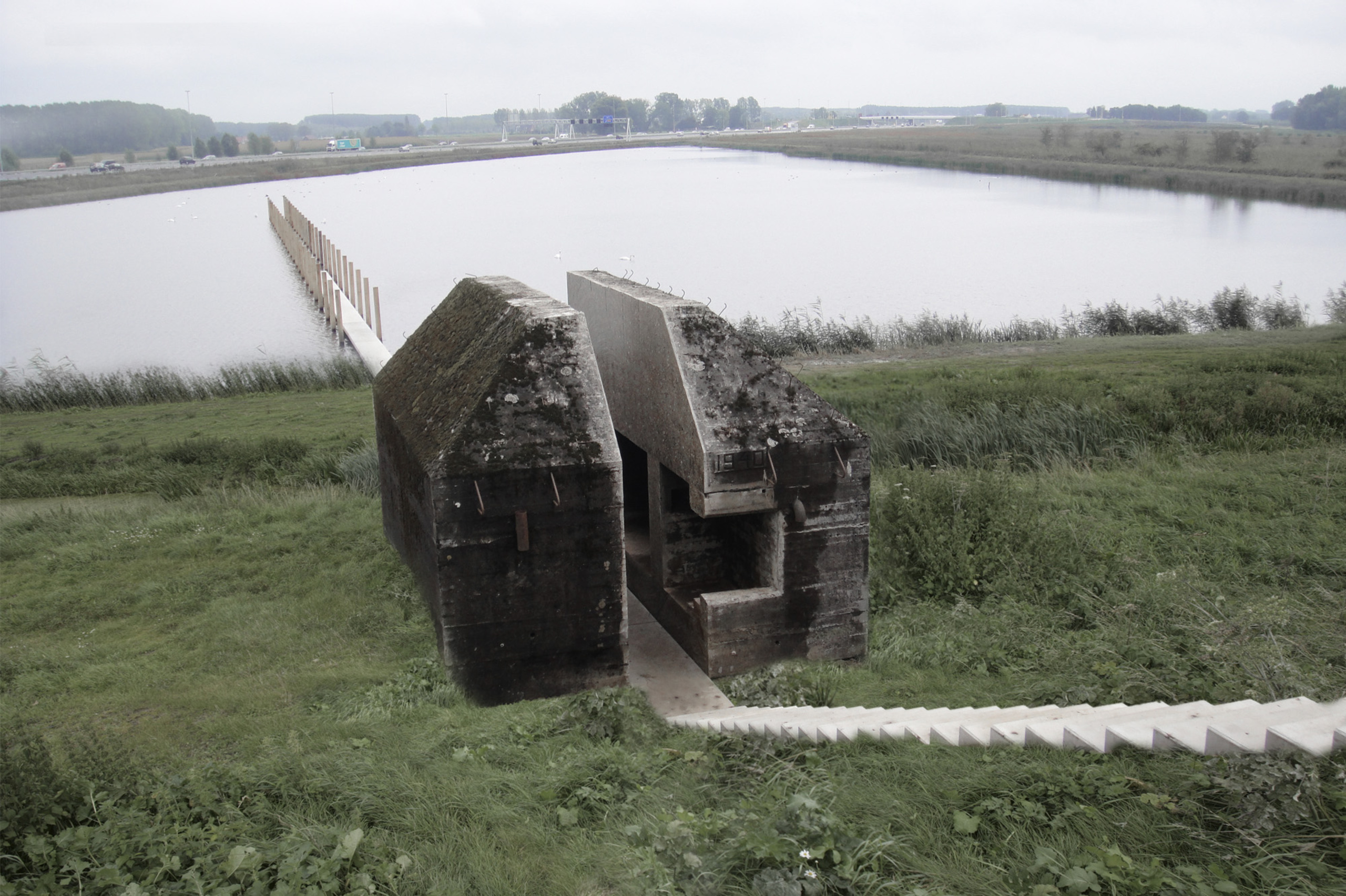 A small concrete WWII bunker next to a body fo water has been cut in half to allow a path to run through it and onto the water.
