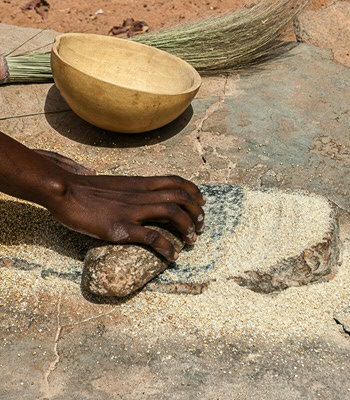 An african woman grinding cereals millet into flour using traditional grindstones, Burkina Faso.